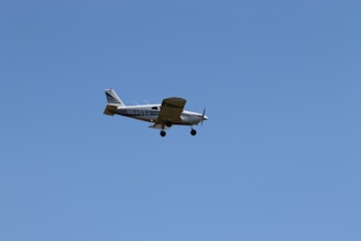A small propeller airplane flying in the clear blue sky, with its landing gear extended and identifiable markings on its body.