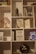 A bookshelf filled with various items, including books, decorative objects, and small plants. Books such as 'Delivering Happiness', 'Platform Revolution', and 'The Lean Startup' are visible. A small potted plant and a decorative tree with red leaves are also present. A dark-colored vase and a vintage-looking object resembling a gong are among the decorative items.