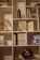 A bookshelf filled with various items, including books, decorative objects, and small plants. Books such as 'Delivering Happiness', 'Platform Revolution', and 'The Lean Startup' are visible. A small potted plant and a decorative tree with red leaves are also present. A dark-colored vase and a vintage-looking object resembling a gong are among the decorative items.