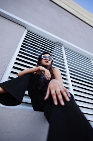 Model wearing bold Maison Madonna sunglasses, standing confidently against a shadowy urban backdrop.