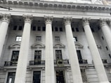 An ornate building facade with large, classical columns and a sign reading 'The Canadian Bank of Commerce.' The architecture features detailed stonework and decorative wreaths hanging on the railings.