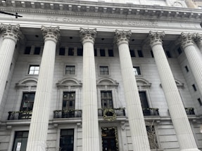 An ornate building facade with large, classical columns and a sign reading 'The Canadian Bank of Commerce.' The architecture features detailed stonework and decorative wreaths hanging on the railings.