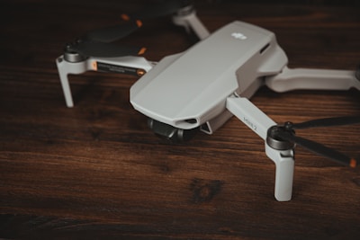 A compact, white drone with black propellers is resting on a wooden surface. The design is sleek and modern, with the model name 'Mini 2' visible on one of the arms.