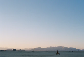 Wide shot of a rider crossing a remote desert landscape under a clear blue sky.