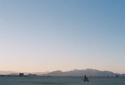 Wide shot of a rider crossing a remote desert landscape under a clear blue sky.