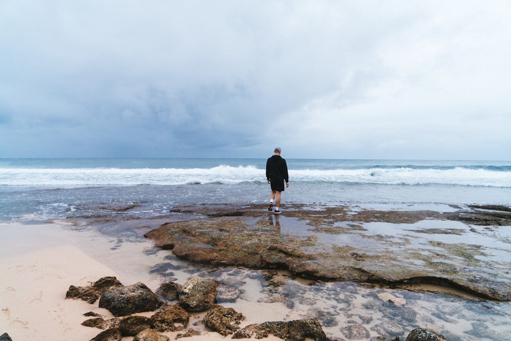 a man standing on top of a rocky beach next to the ocean