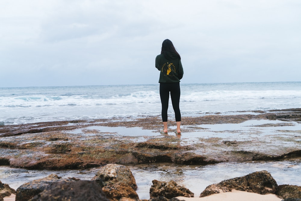 Una mujer de pie en una playa rocosa junto al océano