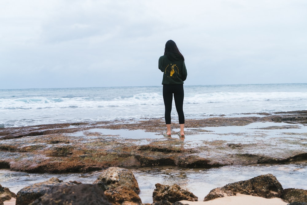 a woman standing on a rocky beach next to the ocean