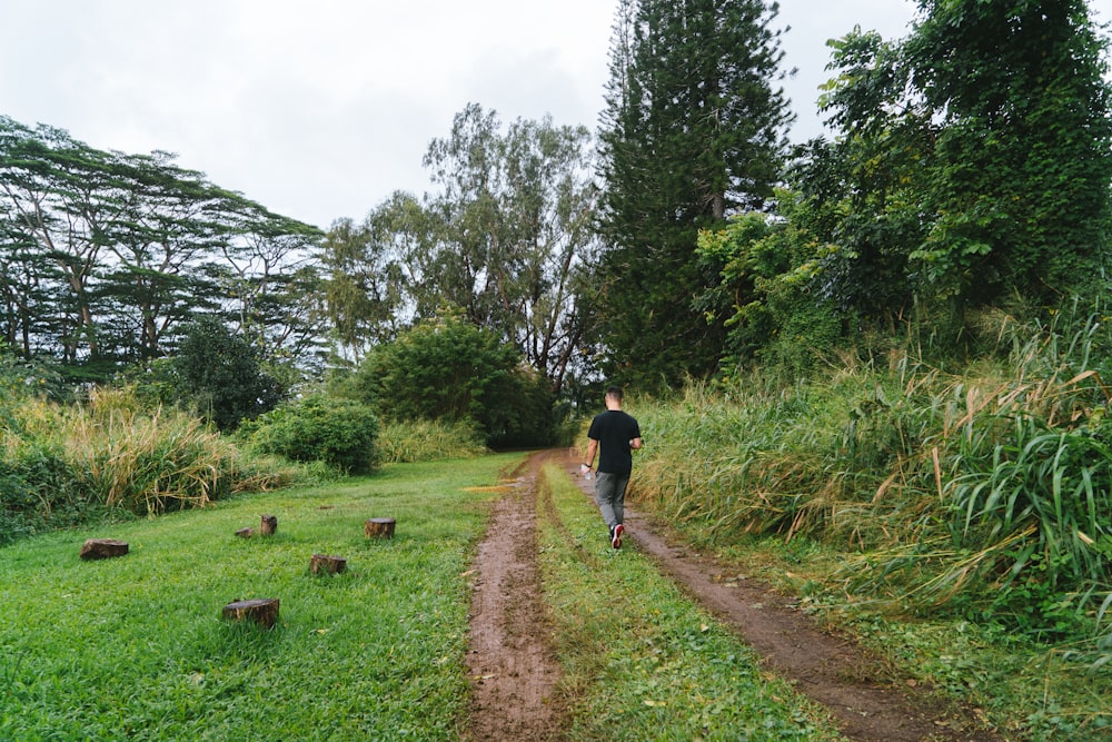 a man walking down a dirt road next to a lush green field