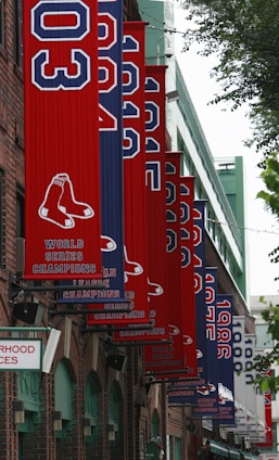 A series of red and blue banners displaying years and the logo of a baseball team hang along the exterior of a brick building. The banners commemorate various championships, with the text 'World Series Champions' and 'American League Champions' visible.