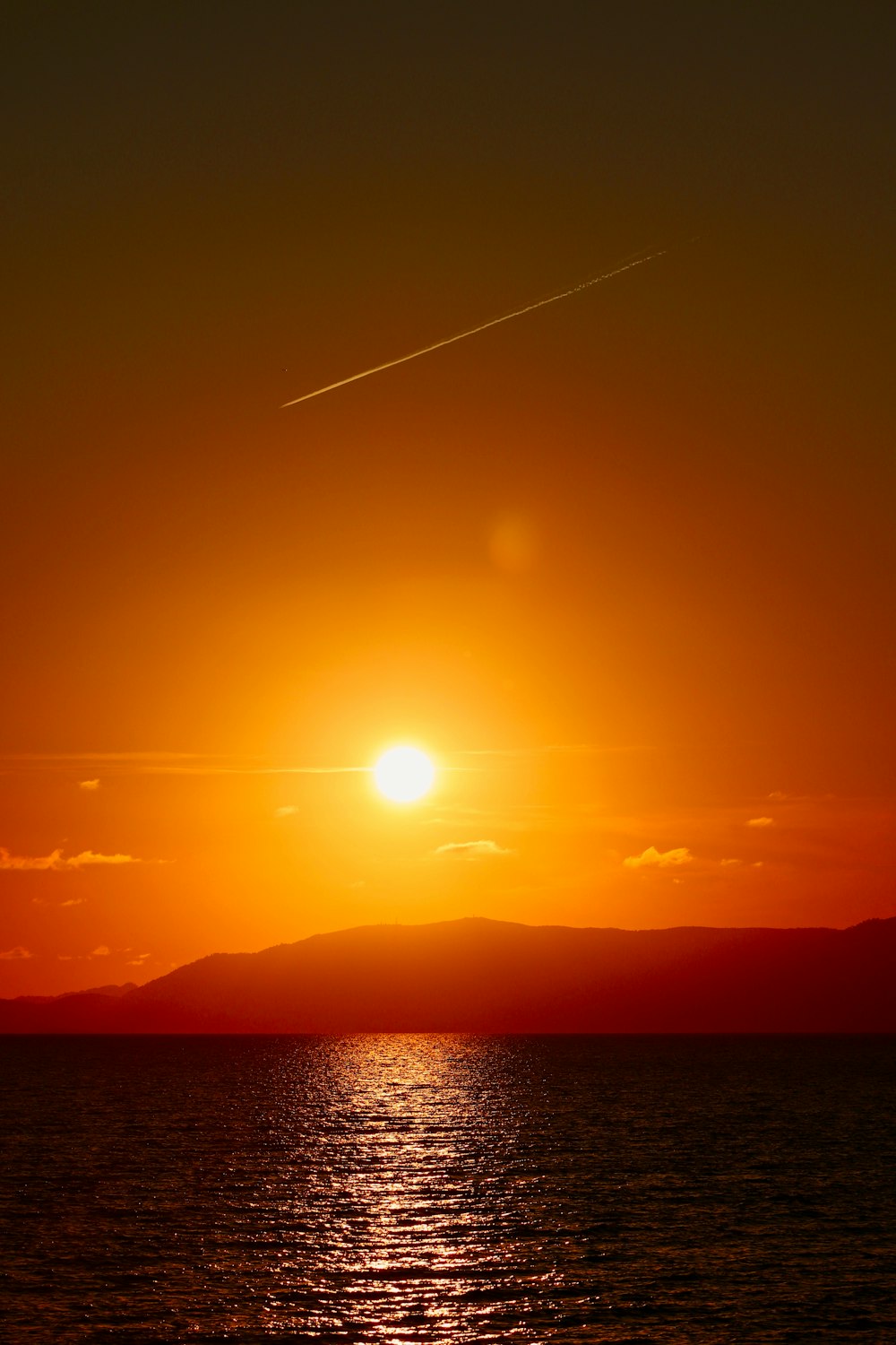 the sun is setting over the ocean with a plane in the sky