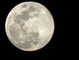 A close-up view of a full moon with visible craters and surface textures against a deep black background.