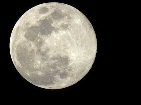 A close-up view of a full moon with visible craters and surface textures against a deep black background.