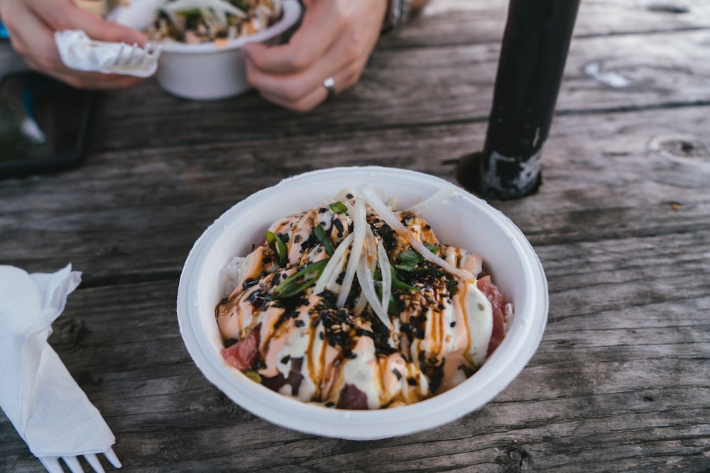 a person holding a bowl of food on a wooden table