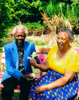 Care staff warmly assisting a smiling senior in the colorful garden setting.