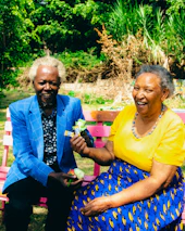 A smiling elderly couple sharing a moment over tea in a peaceful garden.