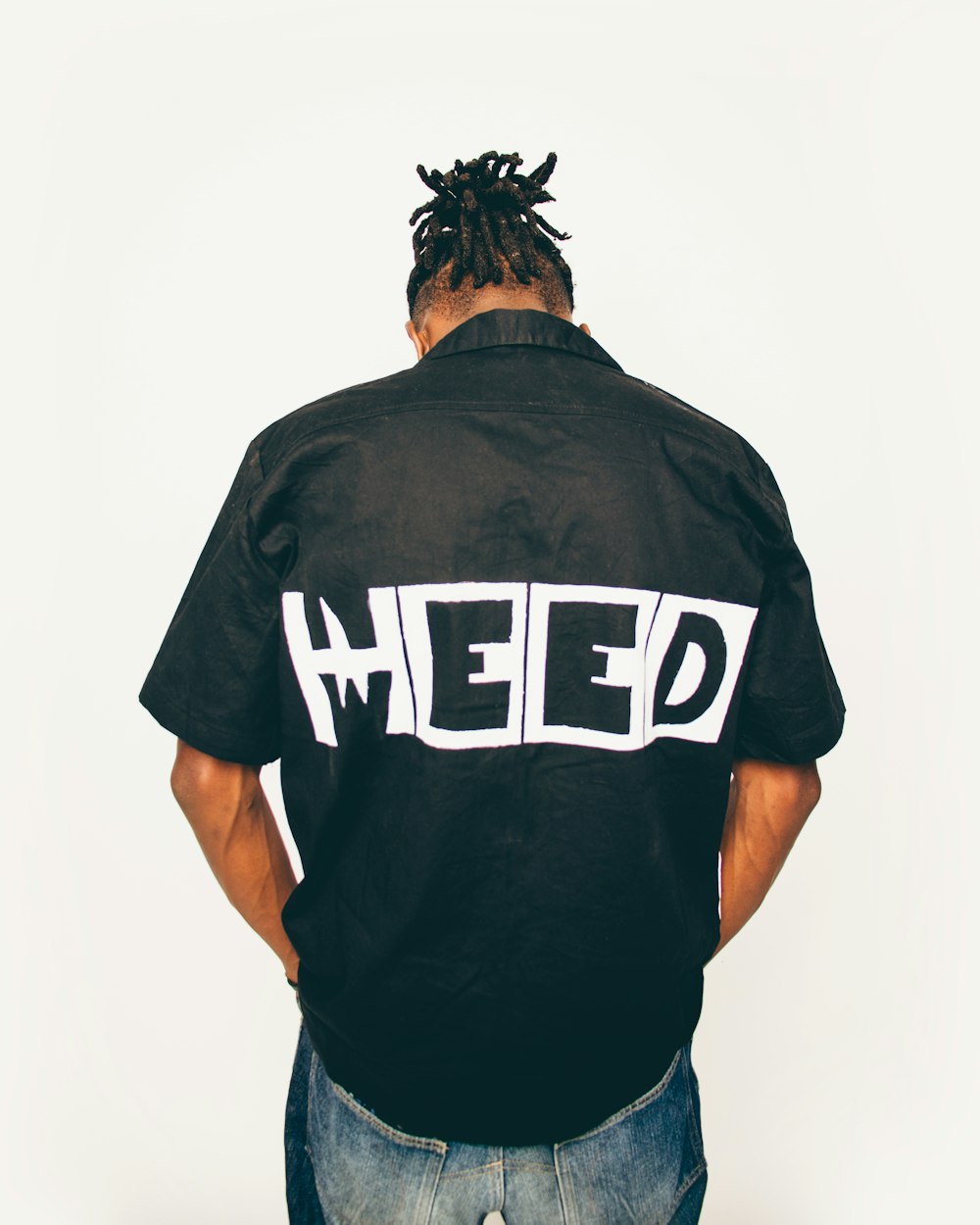 a man with dreadlocks wearing a black shirt with the word heeed on