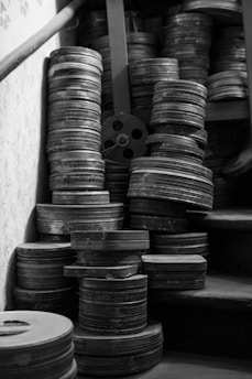 A collection of vintage film reels is stacked haphazardly on wooden stairs. The reels are metallic and aged, suggesting a sense of history or nostalgia.