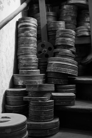 A collection of vintage film reels is stacked haphazardly on wooden stairs. The reels are metallic and aged, suggesting a sense of history or nostalgia.