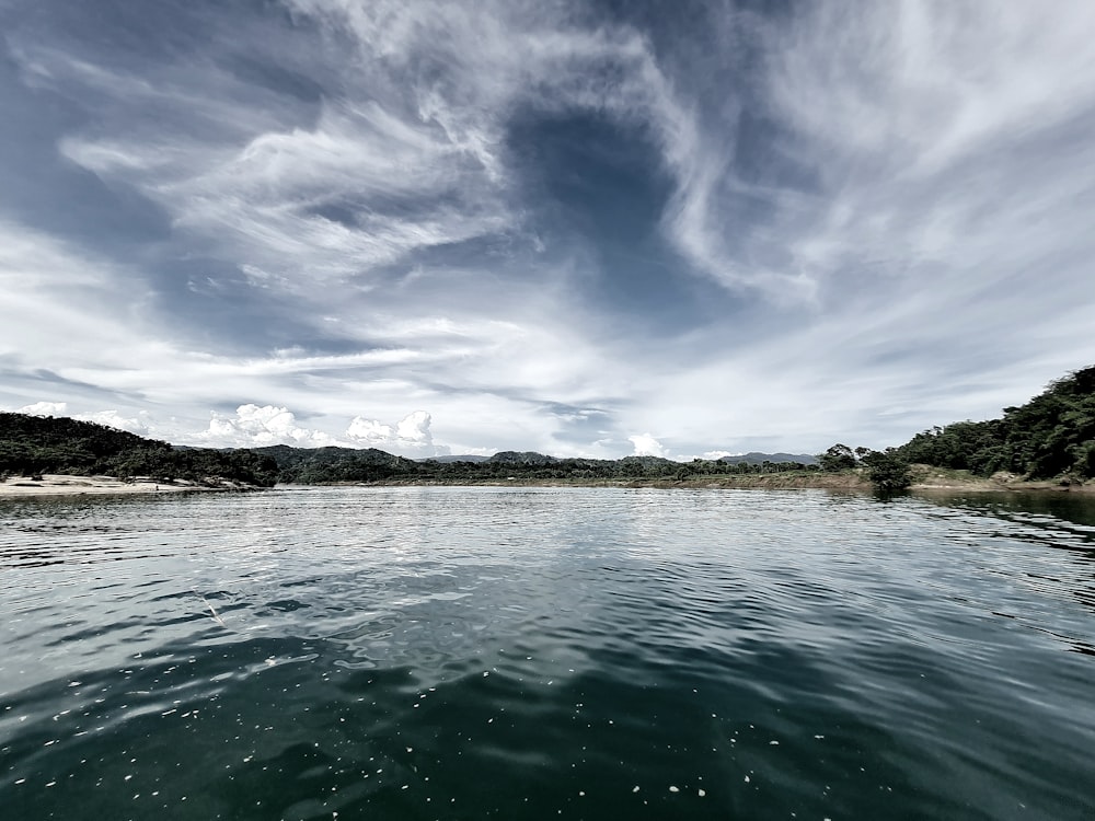 a body of water surrounded by trees and clouds