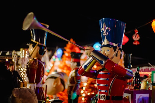 A decorative scene with large toy soldier figures dressed in traditional, colorful uniforms. The main figure is holding a trumpet, set against a vibrant background of lights and festive decorations.