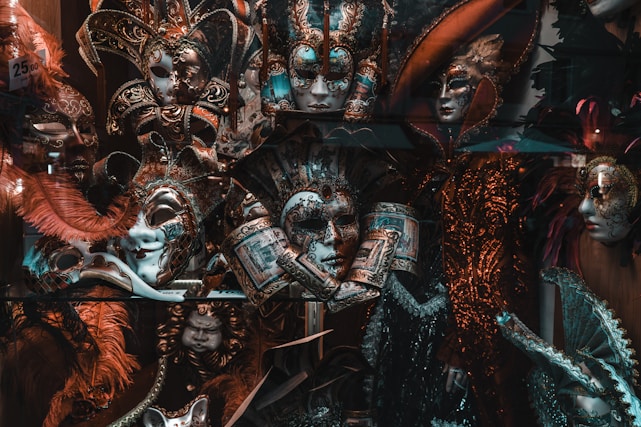 A vivid display of ornate carnival masks adorned with intricate designs, feathers, and embellishments. The masks appear to be part of a collection, demonstrating a variety of artistic styles and colors. Dazzling headpieces with gold, red, and blue tones catch the eye, while some masks feature delicate filigree and painted details.