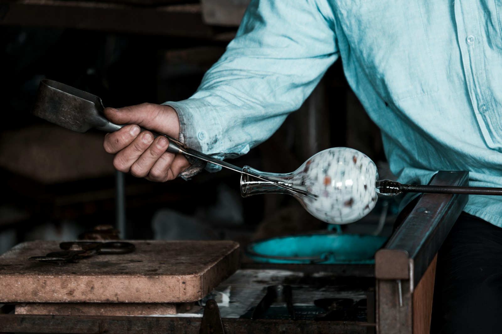 Glassblower rolling a hot gather with tongs at the bench