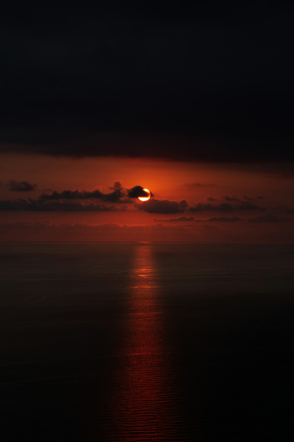 the sun is setting over the ocean on a cloudy day