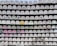 A wall of stacked, identical concrete blocks with circular and square cutouts, some featuring graffiti or colorful paint. The blocks vary in decoration, including smiley faces and abstract patterns. The bottom of the wall has some foliage growing against it.