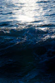 Sunlight sparkling over crystal-clear waves crashing gently on the shore nearby.