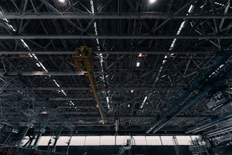 A cinematic shot of a vast warehouse filled with gleaming steel beams under dramatic amber lighting.
