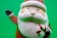 A ceramic or plastic figurine of Santa Claus with a classic red suit and white beard holds a candy cane. It is set against a bright green background.
