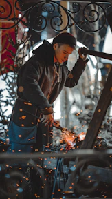 Close-up of hands forging metal on an anvil, sparks flying in a dimly lit workshop.