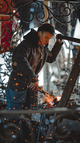 Close-up of hands forging metal on an anvil, sparks flying in a dimly lit workshop.