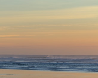 A serene beach at sunrise with soft pastel skies reflecting on gentle waves.