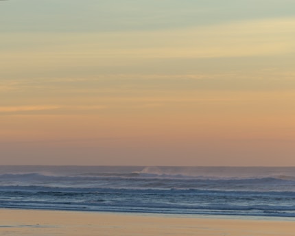 A serene beach at sunrise with soft pastel skies reflecting on gentle waves.