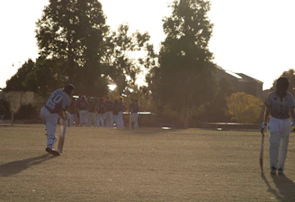 Adult players warming up on a sunny cricket pitch before a match.