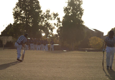 Adult players warming up on a sunny cricket pitch before a match.