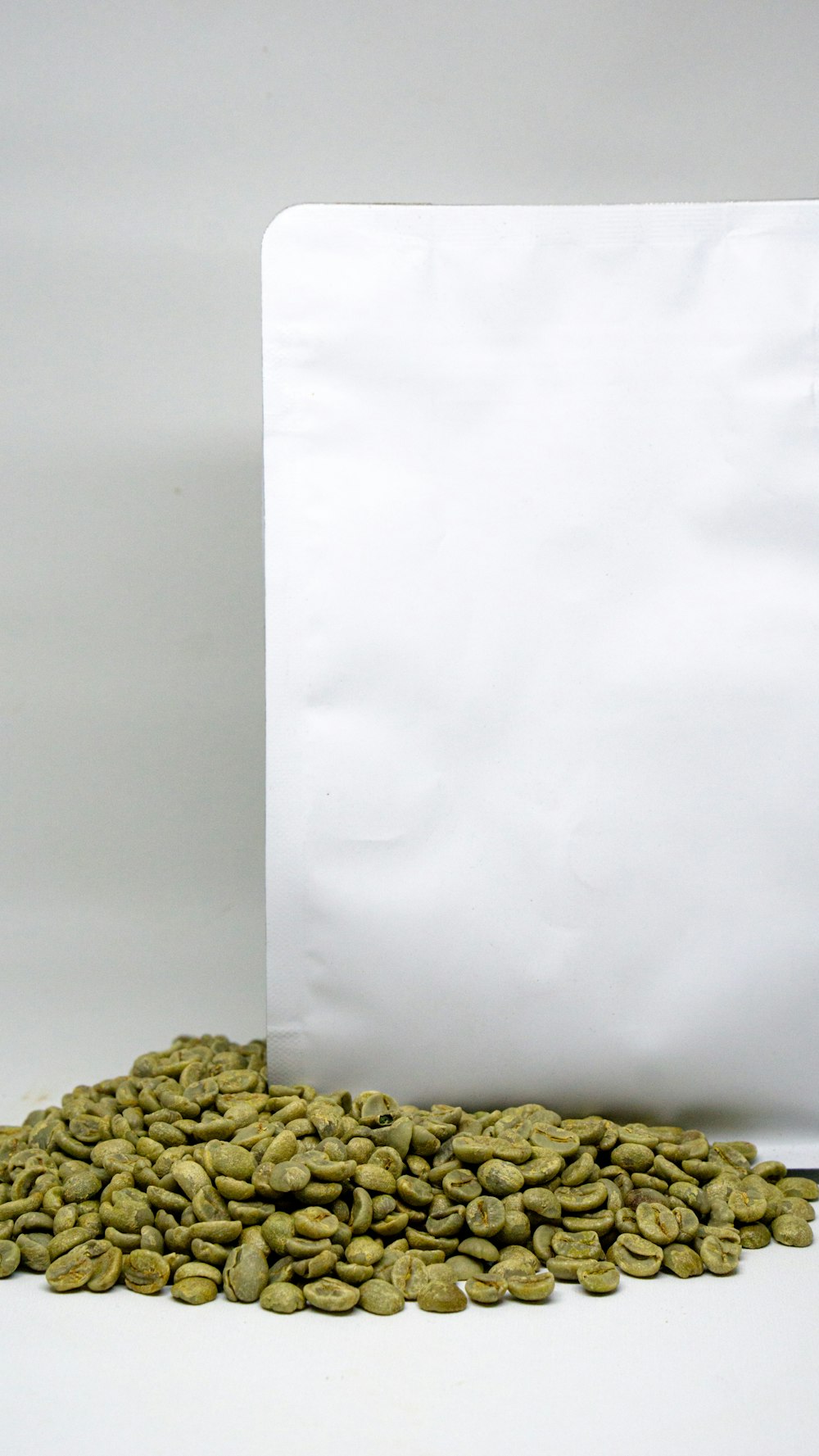 a pile of green coffee beans next to a white bag