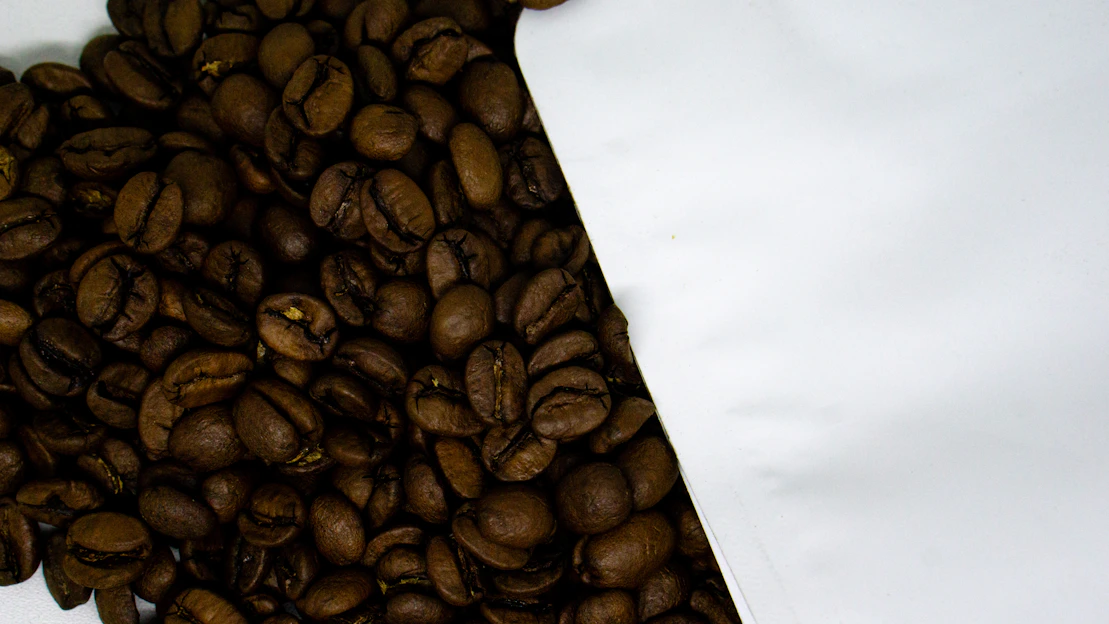 Close-up of a standup coffee pouch with rich roasted beans spilling out on a wooden table.