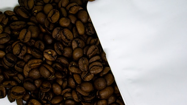 Close-up of glossy dark roasted coffee beans spilling from a burlap sack onto a wooden table.