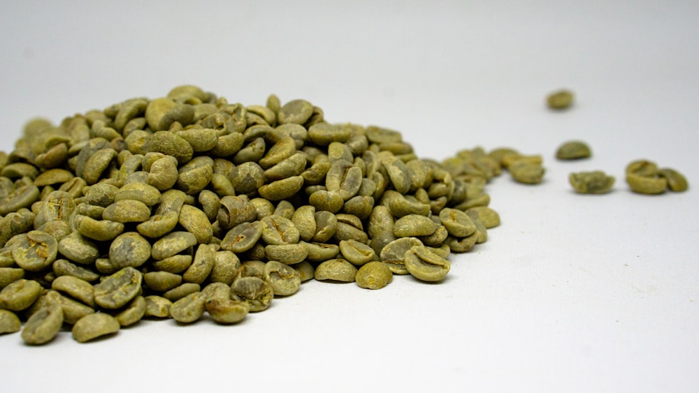 a pile of green coffee beans on a white surface