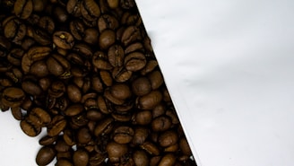 Close-up of freshly roasted dark coffee beans spilling from a burlap sack onto a clean white surface.