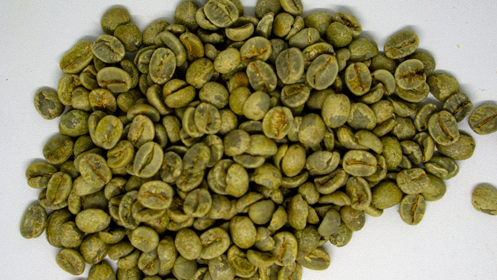 a pile of green coffee beans on a white surface