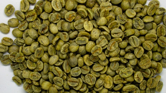 A pile of green coffee beans with a raw, unroasted appearance spread out, showing their distinctive oval shape and pale green coloration.