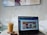 A modern workspace setup featuring a laptop open on a round table. The screen displays a colorful website interface. Beside the laptop is a glass of iced coffee on a coaster and a smartphone. The background reveals a minimalistic wall with abstract art.