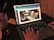 A person is working on a laptop with a design editing software open, displaying a presentation slide featuring two hands typing on a keyboard. The scene is dimly lit, and there is a glass of iced beverage with a straw on the left. A pair of glasses and a mouse are placed beside the laptop.