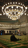 Jamaah praying together peacefully inside Masjid Nabawi under beautiful chandeliers.
