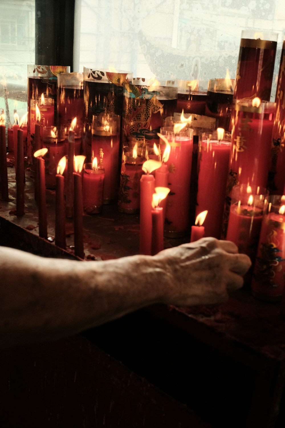 a person's hand is on a table with many lit candles