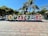Large colorful letters spell out a word in a public plaza with palm trees and other greenery in the background. People are interacting with the letters, and vibrant decorations are strung throughout the area, suggesting a festive atmosphere.